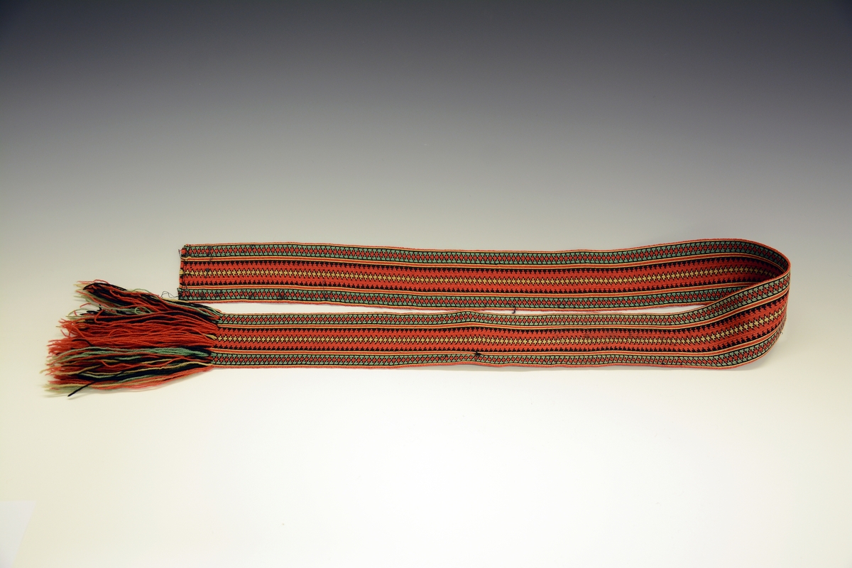 Øst-Telemarksbunad, sydd av Anne Bamle i 1926.TGM-BM.1977:381.A-E
C. Belte. Brikkevevd belte, festet med tråklesting til stakken 1 cm nedenfor baugen. Bredde: 6,5 cm, lengde: 132 cm, hvorav 14 cm frynser som dannes av renningen. Vevd med 63 brikker i mykt 4-tråds ullgarn i farvene rustrødt, gult, grønt og sort med den den rustrøde som dominerende i  midtpartiet og grønne striper på sidene. 1 trykkapp og 3 hekter holder beltet sammen på venstre side 12 cm fra midten, enden med frynsene faller fritt ned.