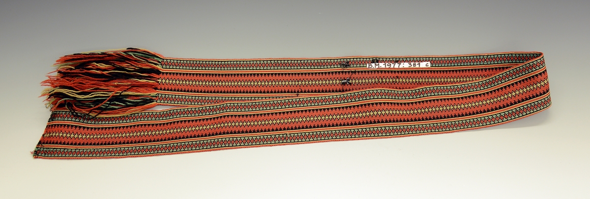 Øst-Telemarksbunad, sydd av Anne Bamle i 1926.TGM-BM.1977:381.A-E
C. Belte. Brikkevevd belte, festet med tråklesting til stakken 1 cm nedenfor baugen. Bredde: 6,5 cm, lengde: 132 cm, hvorav 14 cm frynser som dannes av renningen. Vevd med 63 brikker i mykt 4-tråds ullgarn i farvene rustrødt, gult, grønt og sort med den den rustrøde som dominerende i  midtpartiet og grønne striper på sidene. 1 trykkapp og 3 hekter holder beltet sammen på venstre side 12 cm fra midten, enden med frynsene faller fritt ned.