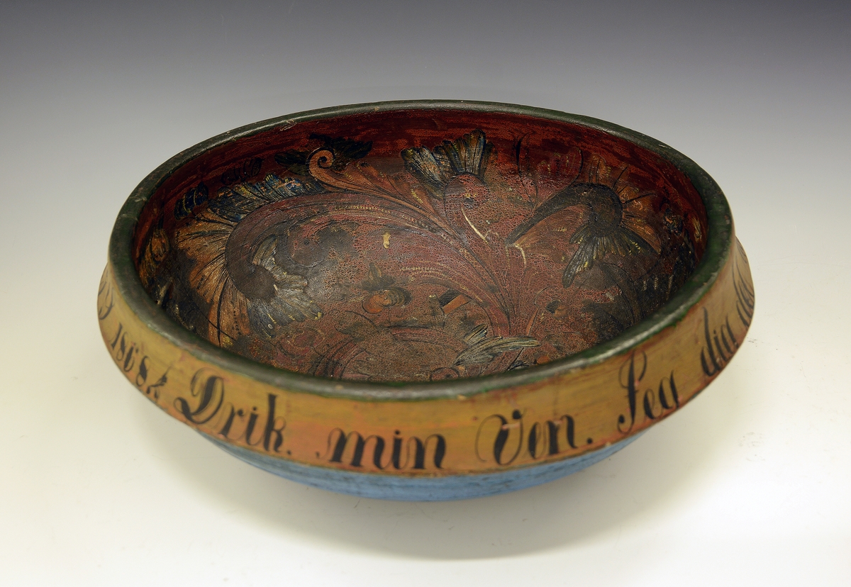 Rosemalt ølbolle. Fra protokollen: Ølbolle, svarvet med sterkt utstaaende ribbe, hvorfra en kant böier ind. Nyere overmaling, utenpaa malt lyseblaa med minjerød kant, hvorpaa indskriften: "Drik min Ven. Jeg dig det Under. Pust imelem og Giv dig stunder. G.G.S. 1868". Indeni er paa gulbrun bund  malt svære roser i c-oplæg og nærmest i Luraasstil; farver: rødbrunt, grønt, blaat, hvitt, gult; sort skrafering. Bollen er kinget.