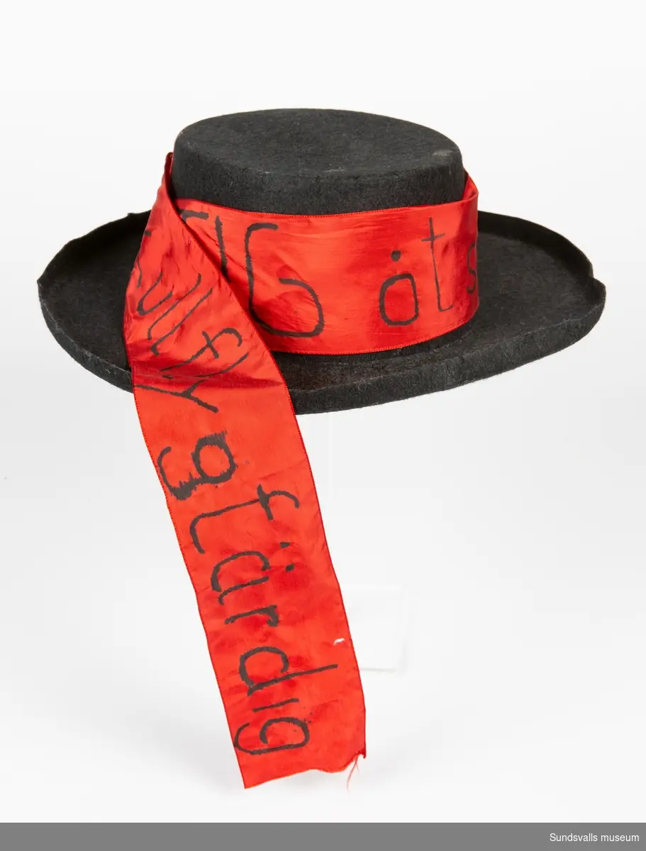 Svart hatt med bred kant. Ett rött band är fastsytt på sidan med skriften " Stig åt sidan 63:ans kull flygfärdig"