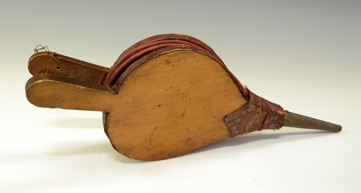 Ovnsbelg. Fra protokoll: Omnsbelg (omspustar)  i uvand blekkpipe. pæreforma bokvedbynir, raudt saffiand skinn, nagla med salmakarstiftur. Lengd med skaft og pipe 38,5 cm.