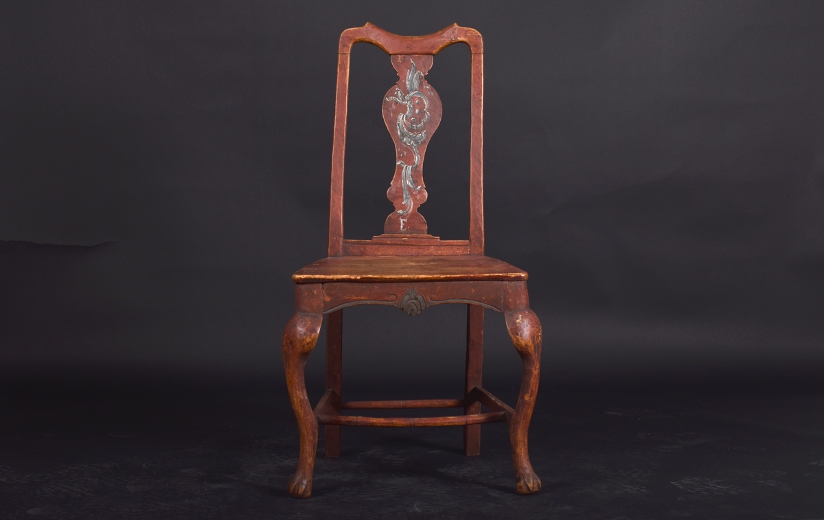 Stol av björk och furu, på fyra svängda ben. Ryggen har en mittbricka i balusterform. Stolen är målad i mörkt rött och ryggbrickan har målad dekoration i rokokostil i grått och vitt.