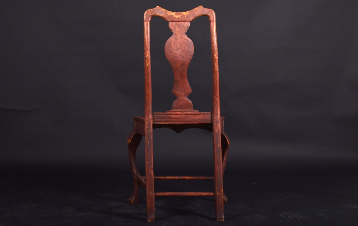 Stol av björk och furu, på fyra svängda ben. Ryggen har en mittbricka i balusterform. Stolen är målad i mörkt rött och ryggbrickan har målad dekoration i rokokostil i grått och vitt.