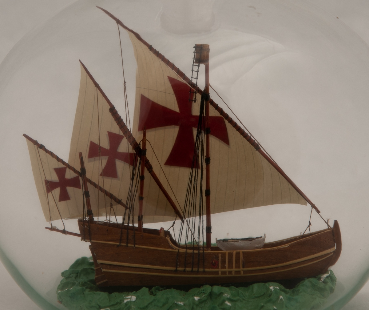 Flaskeskute: "Nina" , en karavell. Skuta er inne i en kuleformet flaske. Skuta har tremaster med latinerseil , som har påmalte røde malteserkors på seg. Grønn sjø med hvite topper. Hørte til Columbus` flåte. Ble på tilbaketuren fra Amerika rigget om med råseil for å kunne holde tritt med "Pinta".