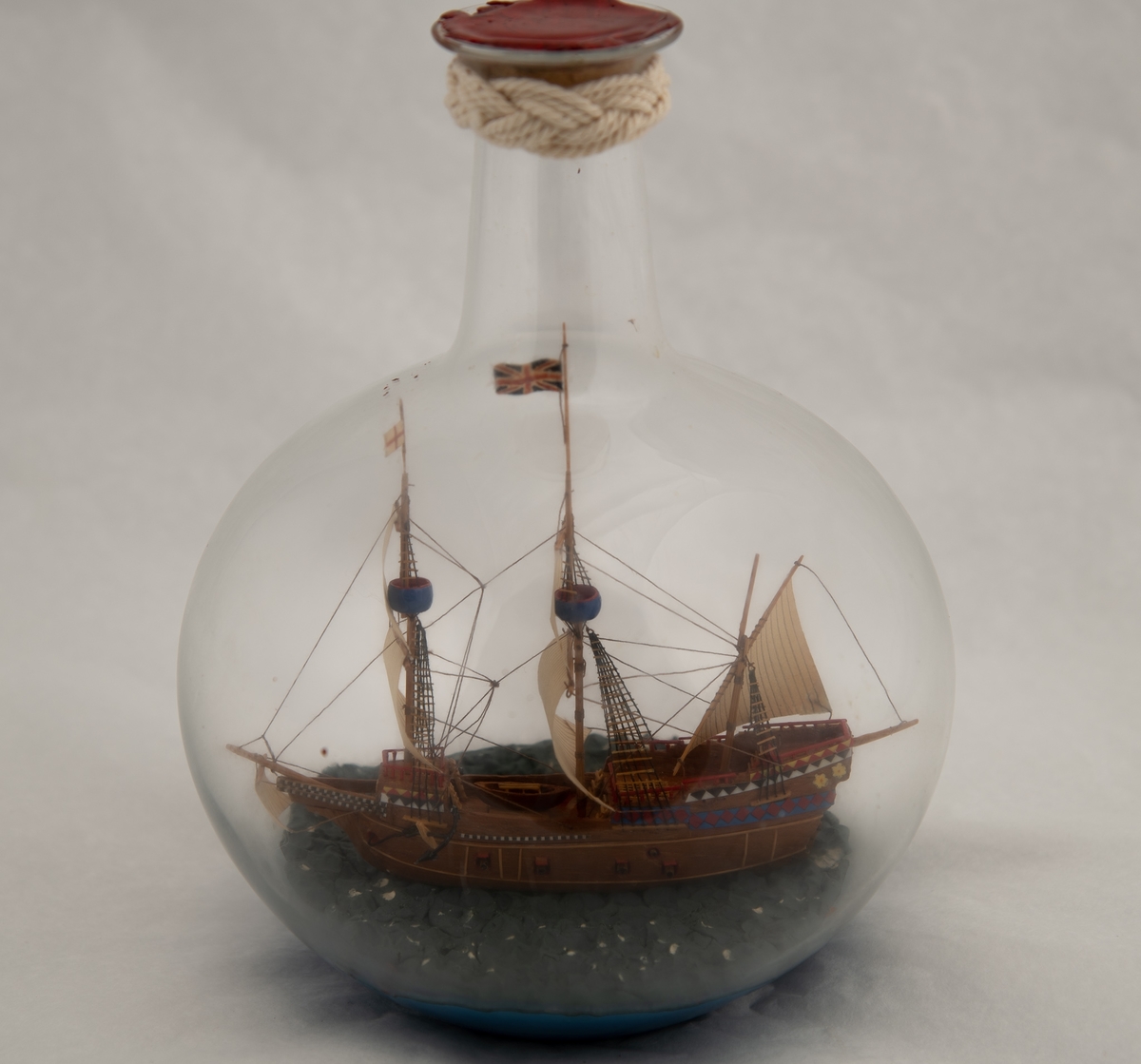 Flaskeskute; "Mayflower", en tremastet galleon fra 1615 , tok i l620 102 utvandrere fra England til Amerika. Symbol for frihetsrettigheter og religiøs toleranse.  Kuleformet glassflaske. Brunt skrog , dekorert i akterspeilet med border i blått , rødt , sort , hvitt og gult. Britisk flagg.