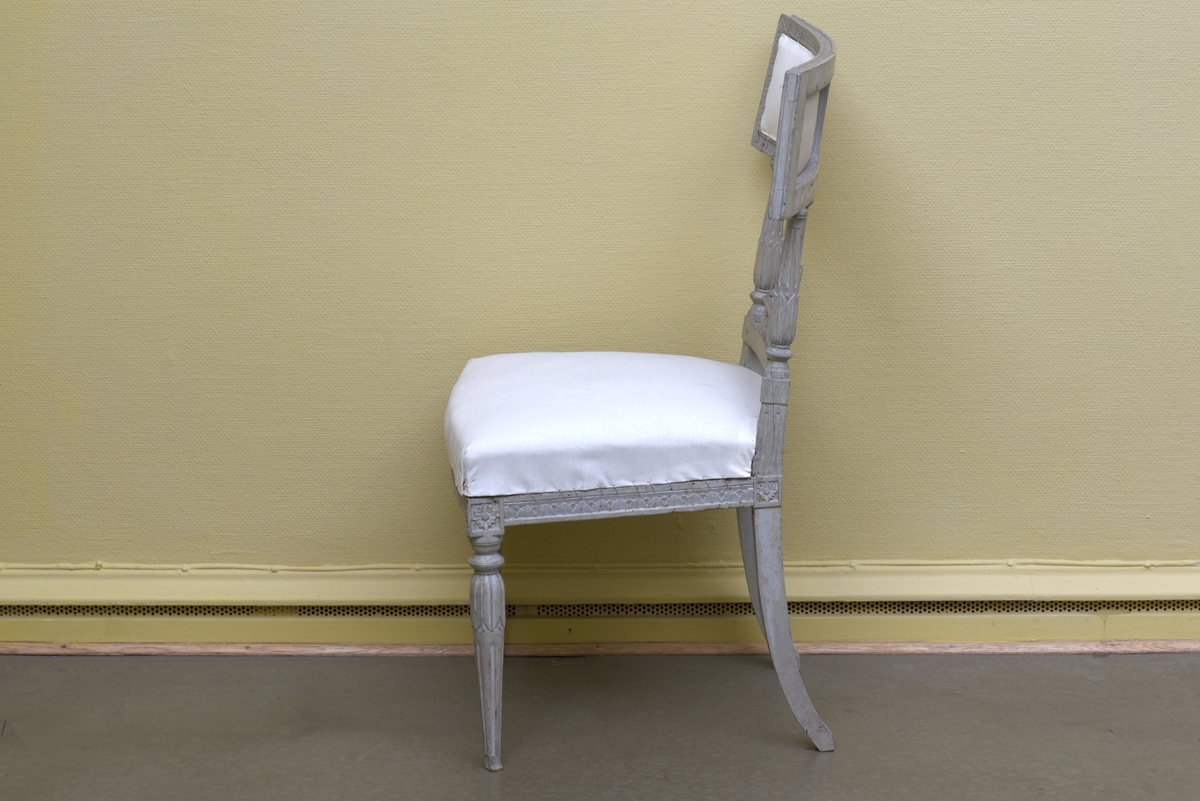Gråvit stol i gustaviansk stil av björk på runda, avsmalnande ben. Benens övre del är dekorerade med bladkrans. Den främre sargen är något svängd och dekorerad med en äggstavslist. Den rektangulära ryggbrickan bärs upp av totalt fem, tre mindre och två större, ståndare. Ryggbrickans ramvirke är dekorerad med äggstavslist. Stolen är provisoriskt klädd på sits och i rygg med ett vitt bomullstyg.