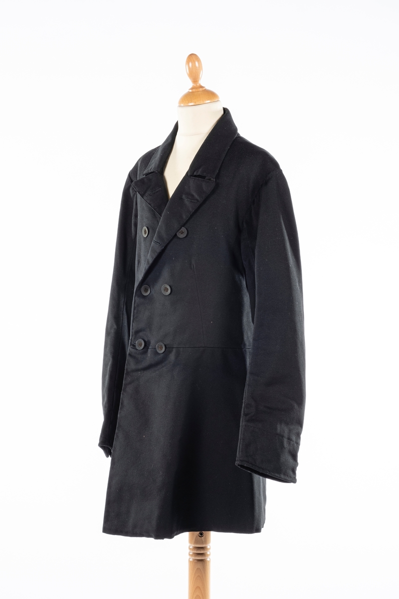 Dobbelt spent frakk som kneppes med fire knapper på hver side. De øverste kan ikke kneppes. Knappene er kledd med silke med fløyelsornament i midten. Hempe i nakkelinning. Det er splitt med legg fra livet og ned, med en knapp over splitten på hver side. Det er også to knapper lenger ned i splitten, og en knapp på hver mansjett. Frakken er foret.