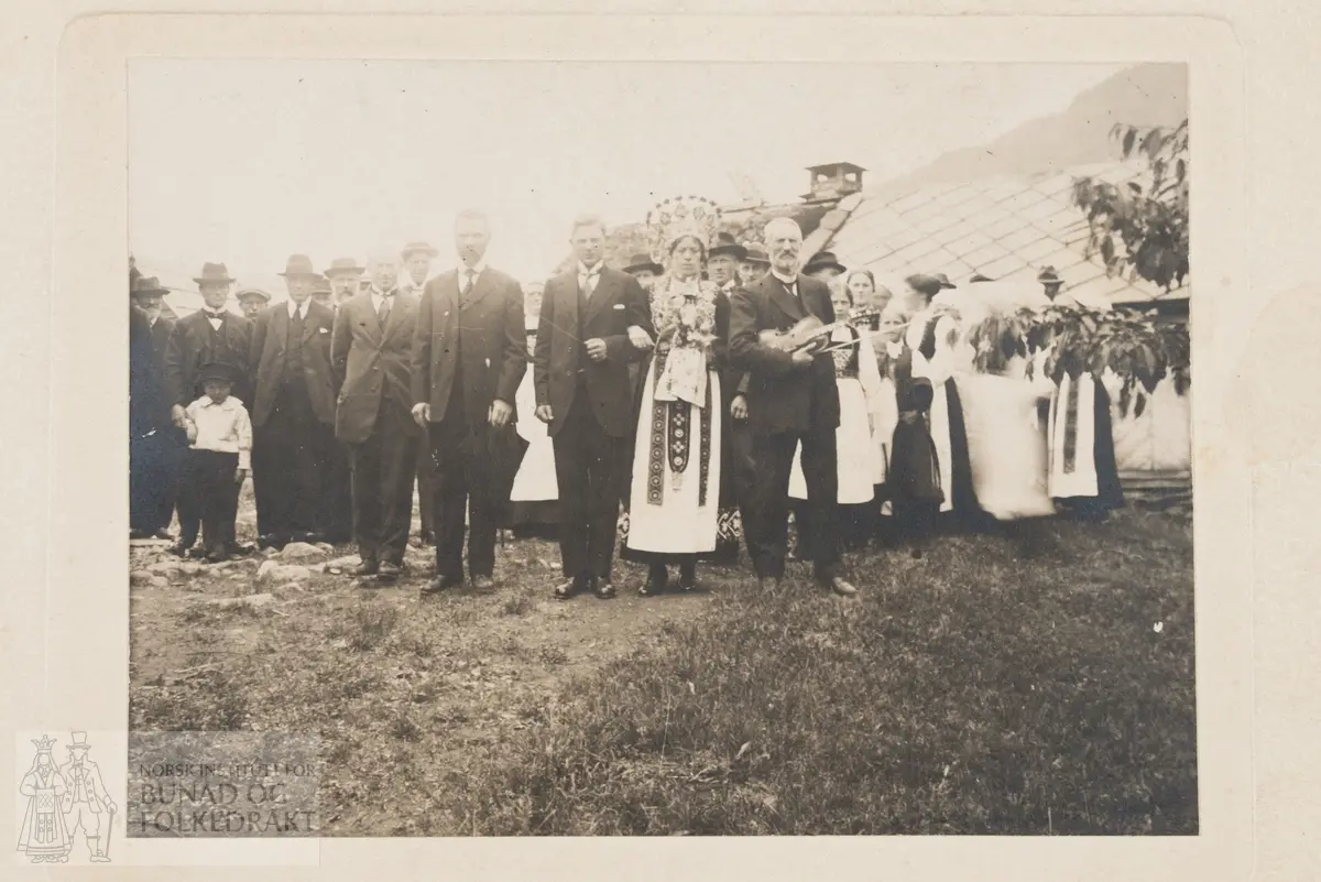 Gruppebilde, bryllup. Brud med perlekrone, brudgom, spelemann med hardingfele. Tidlig 1900-tall. Spelemann er Svein Lutro (1850-1929).
Skrevet bakpå: Til Guri Kjerland Granvin. Fra Anna og Halldor Opedal.