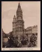 På bilden syns en grupp motorcyklister på ett torg i Frankrike. Bakgrunden domineras av ett stort klostertorn.