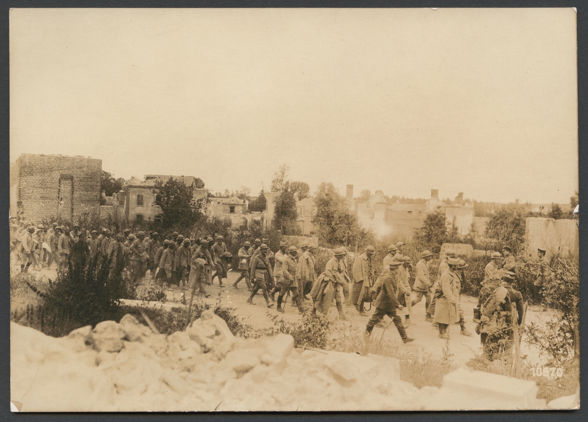 Bilden visar franska krigsfångar på marsch genom ruinerna av en förstörd by.