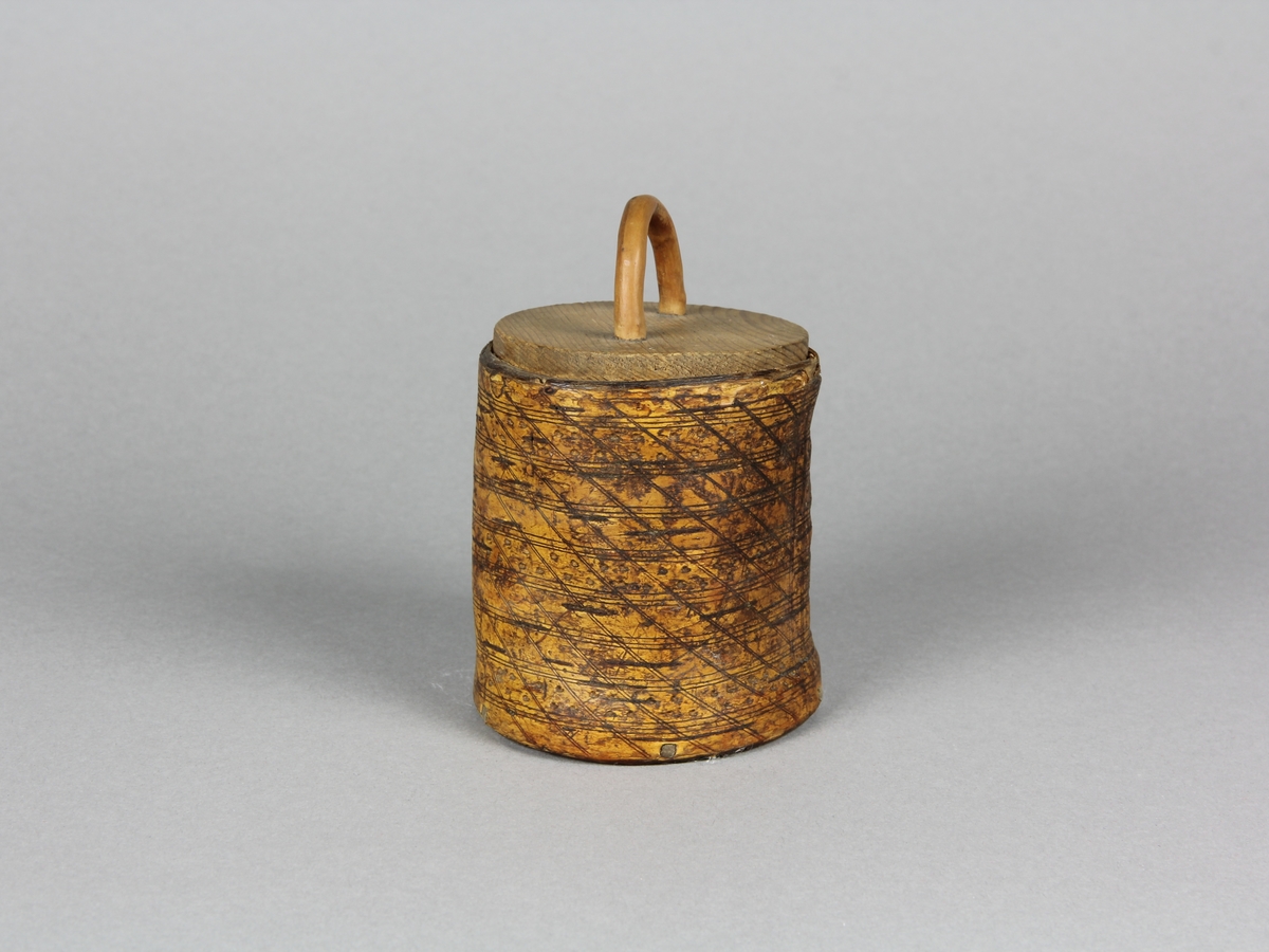 Snusburk, cylinderformad av hel näver med lock och botten av furu. Nävern ornerad i rut- och prickmönster. Näverändarna fästa genom att de tampats och flätats ihop. På locket tvärgrepe av enträ som kilats fast från undersidan. Snusrester i botten.