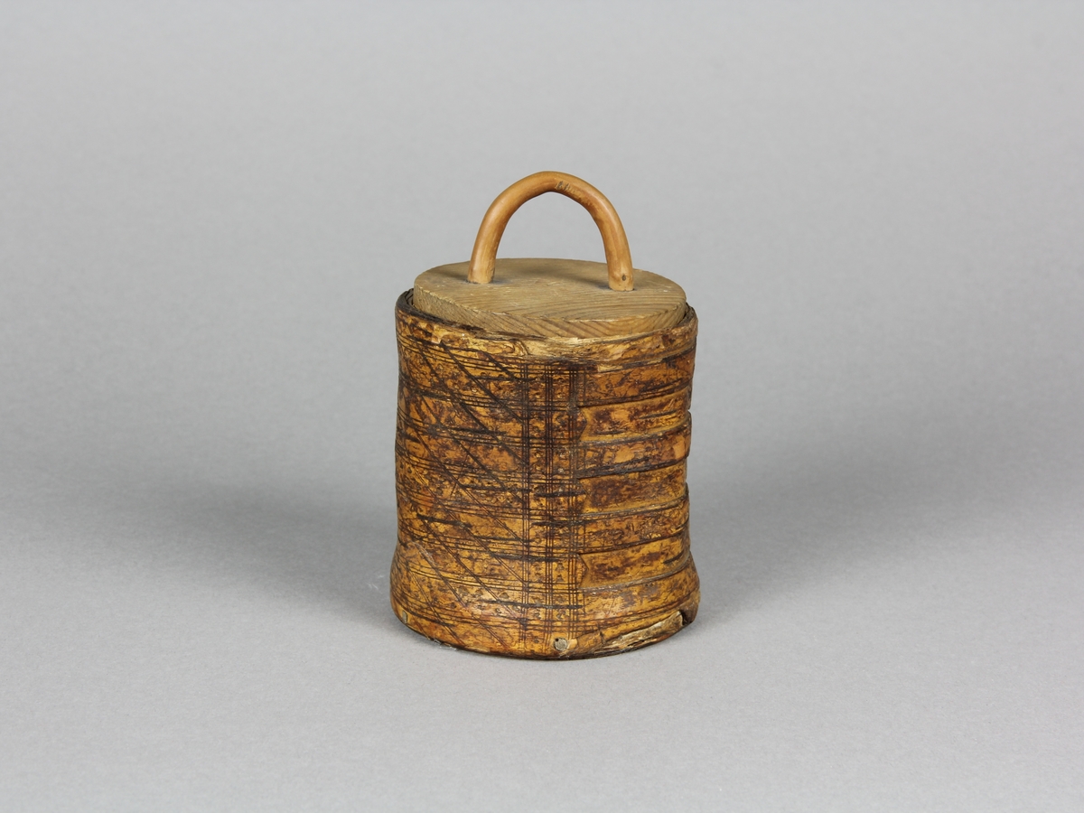 Snusburk, cylinderformad av hel näver med lock och botten av furu. Nävern ornerad i rut- och prickmönster. Näverändarna fästa genom att de tampats och flätats ihop. På locket tvärgrepe av enträ som kilats fast från undersidan. Snusrester i botten.