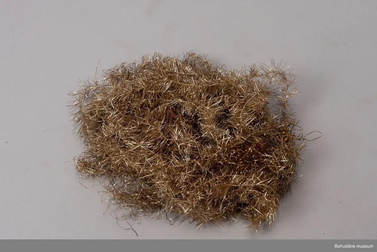 Låda av brun papp. På locket påklistrad,delvis bortsliten etikett med text: "Herman Radyn Uddevalla". Lådan innehåller: 19 st. julgransljushållare, glitter i silver, glitterband i guld, 7 st. julgranskarameller av papper, 1 toppstjärna, 12 st. hjärtan av papper i olika färger, 6 st. små glasbollar i sytråd, svenska flaggor i tråd, 12 st. svenska flaggor med järntråd,