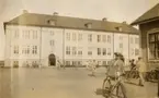 Soldat vid cykel utanför regementsbyggnad.