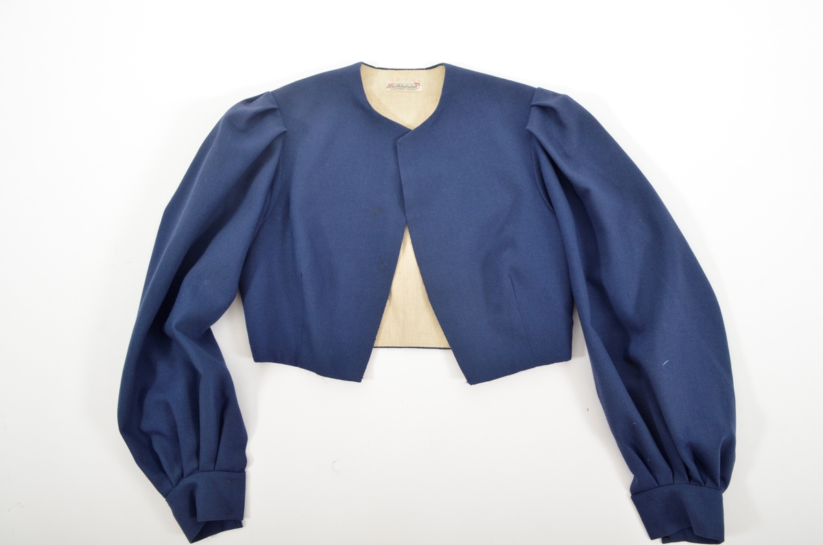 Grafferbunad med raudt damaskvove ulltøy i livet, og blått toskaftvove ulltøy i stakken. A. Livet har opning framme festa saman med tre hekter og krokar. Saum midt bak, og med to svinga ryggsaumar. Fóra med ubleikt halvlin.
Stakk i toskaft-vove ulltøy, brodert med ullgarn i forskjellige fargar. Rosemotiv. Den er foldelagt. Brei skonnering av svart bomulltøy i  nedrekanten.
B. Jakke i blått toskaftvove ulltøy. Opning midt framme med tre hekter og krokar til lukking. Eit snitt på kvar side. Erme er foldelagt oppå skuldera og nede ved ermekragen. 
C. Lue, pullue, i same tøy og broderi som stakken. Fóra med ubleikt halvlin. I nedrekant av pullen løpegang med rynka strikk. 
D. Lomme i same tøy og broderi som stakken. Sølvforgylt lommelås.