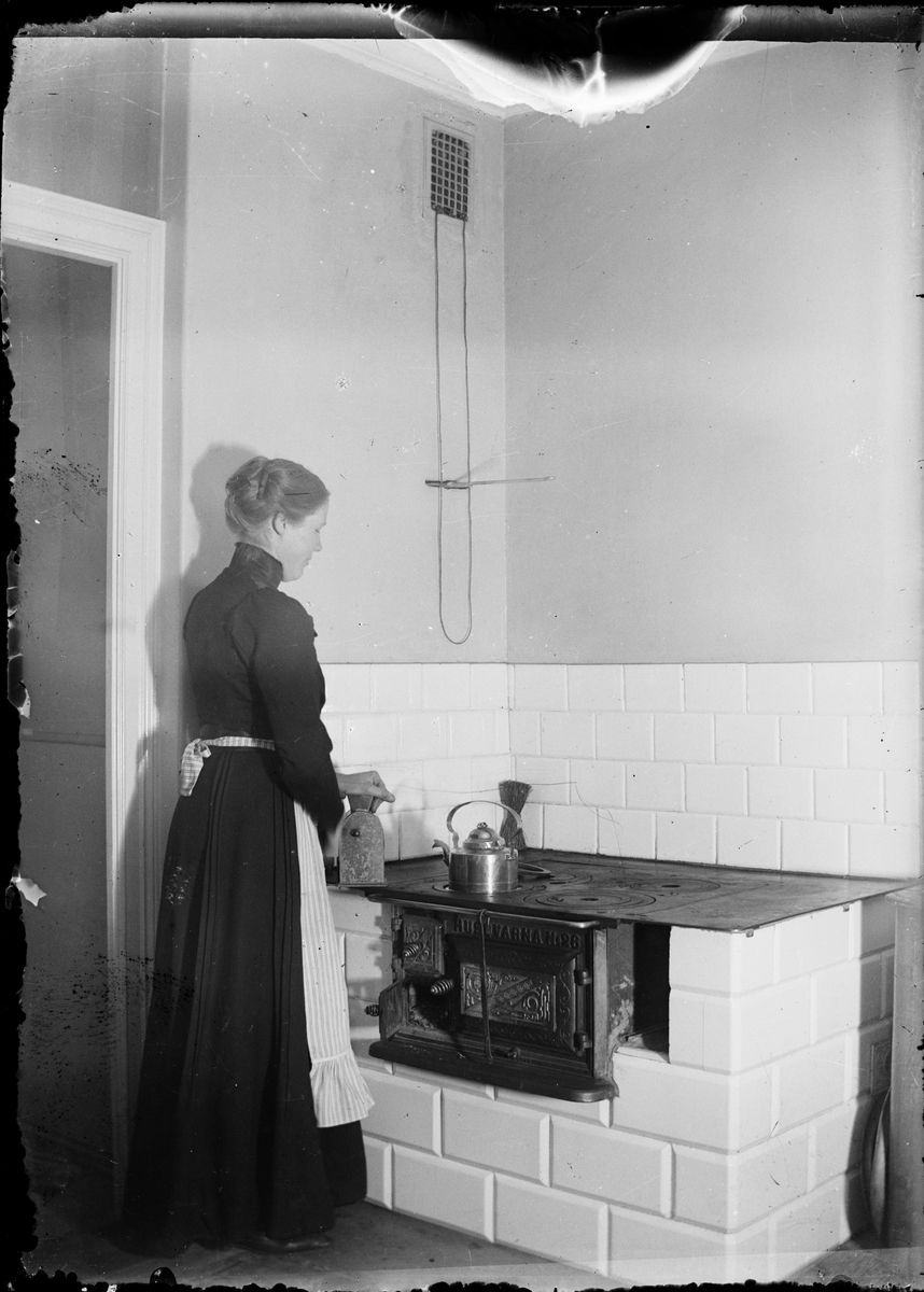 Ruth Skötsner står vid vedspisen och mal kaffe, Östhammar, Uppland