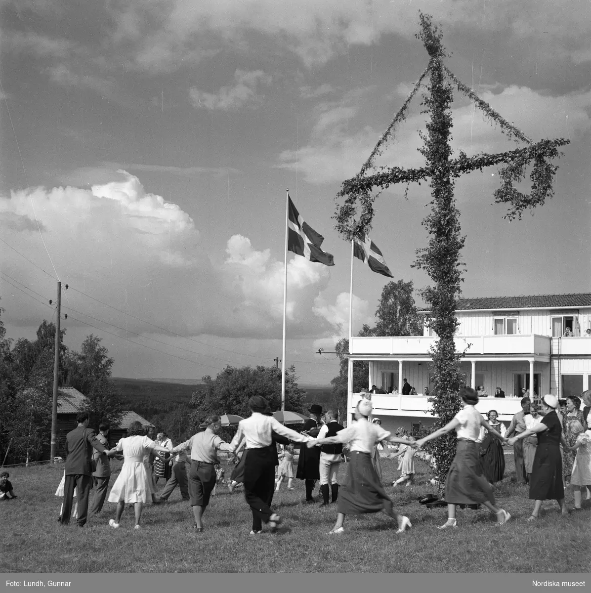 Motiv: Lerdalshöjden ;
Porträtt av en flicka som håller blommor, vuxna och barn dansar runt en midsommarstång, tre män i folkdräkt spelar fiol vid en midsommarstång.