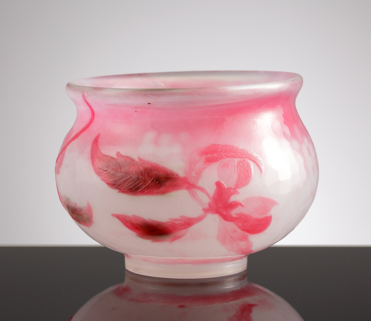 Skål med opaliserande vitt glas och mörkrosa överfång. Dekor av svagt stiliserad kvist med äppelblom. Gröna fläckar på insidan bakom bladen.