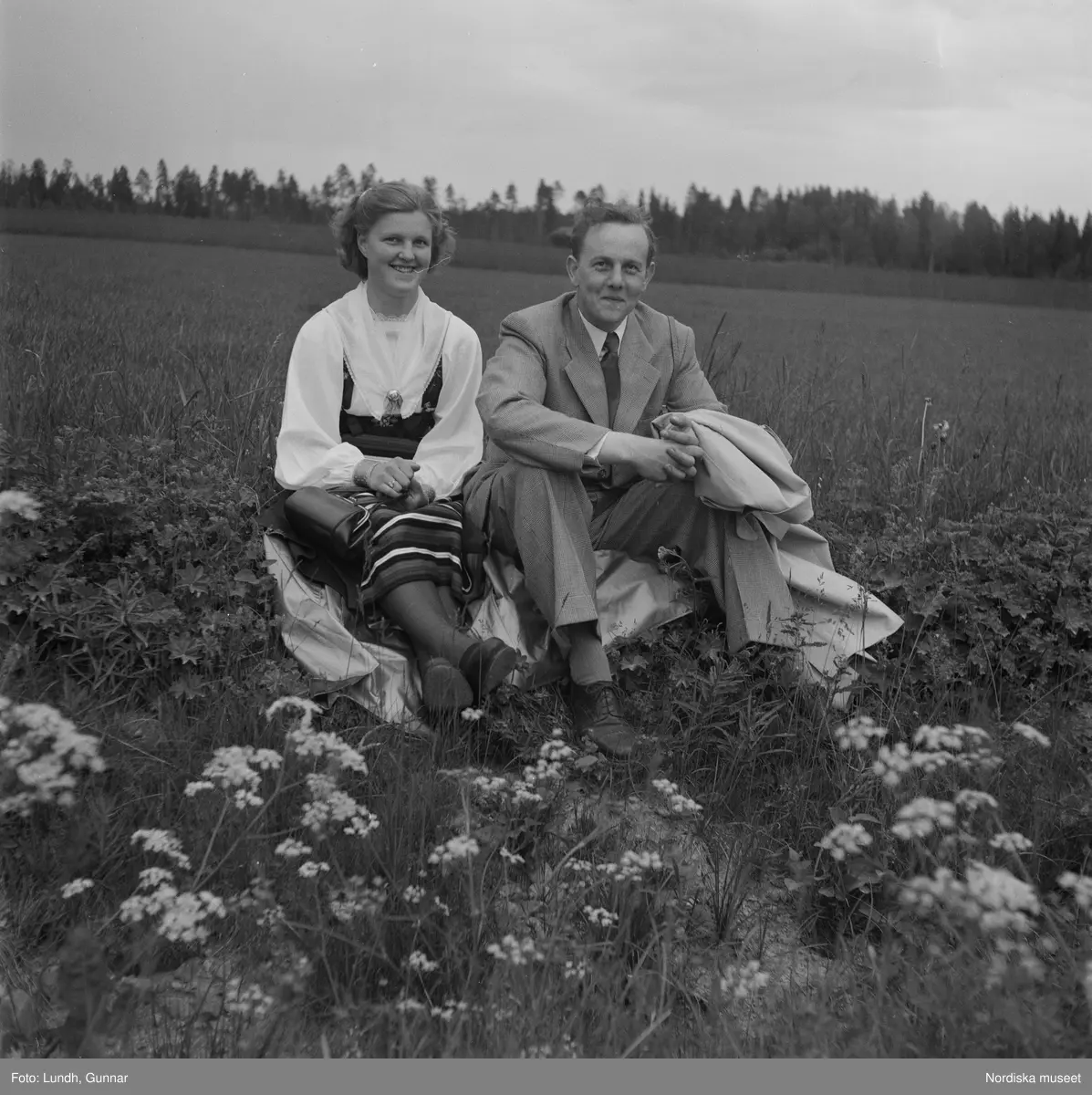 Motiv: (ingen anteckning) ;
Porträtt av en kvinna i folkdräkt och en man som sitter på marken, män och kvinnor i folkdräkt går i ett proccesionståg med flaggor och kvinnor bär en lövad girlang, människor åker på en hästdragen vagn, en folksamling går i ett processionståg.