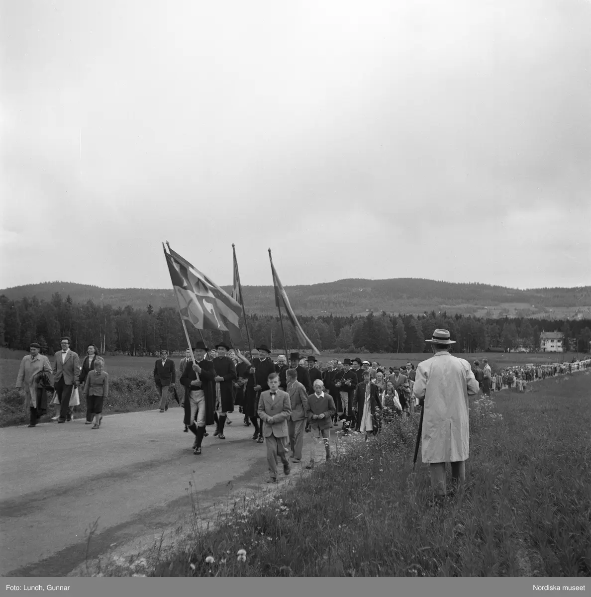 Motiv: (ingen anteckning) ;
Porträtt av en kvinna i folkdräkt och en man som sitter på marken, män och kvinnor i folkdräkt går i ett proccesionståg med flaggor och kvinnor bär en lövad girlang, människor åker på en hästdragen vagn, en folksamling går i ett processionståg.