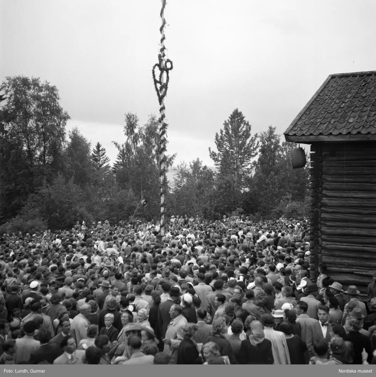 Motiv: (ingen anteckning) ;
En folksamling står kring en midsommarstång, en folksamling vid ett hus, en kyrkbåt ros av kvinnor och män i folkdräkt, en folksamling står vid en brygga med en kyrkbåt.