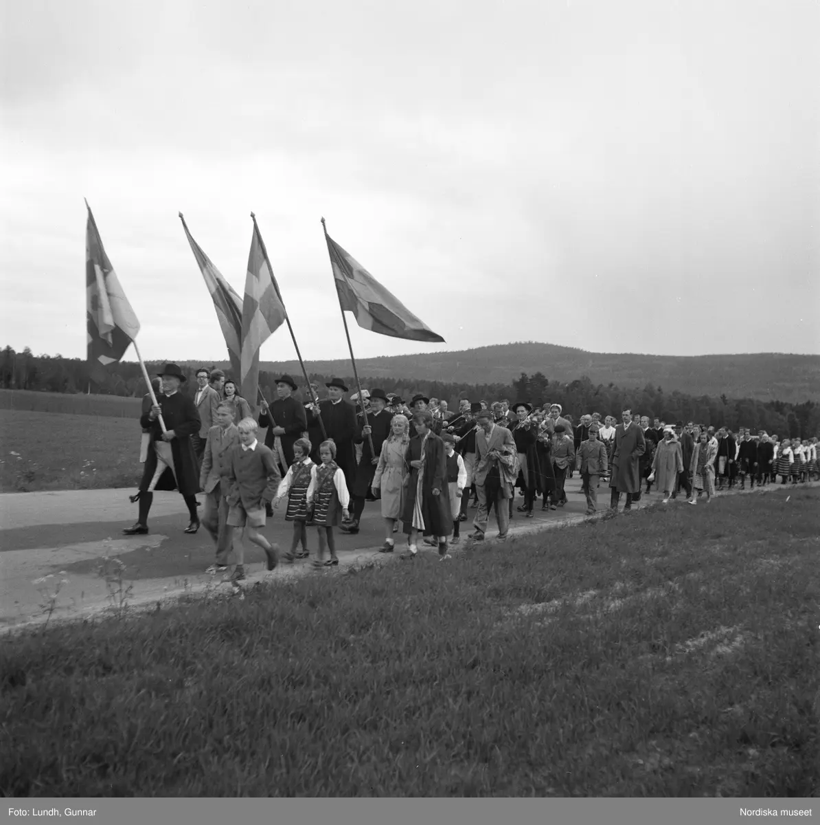Motiv: (ingen anteckning) ;
Porträtt av en kvinna i folkdräkt och en man som sitter på marken, män och kvinnor i folkdräkt går i ett proccesionståg med flaggor och kvinnor bär en lövad girlang, människor åker på en hästdragen vagn, en folksamling går i ett processionståg.