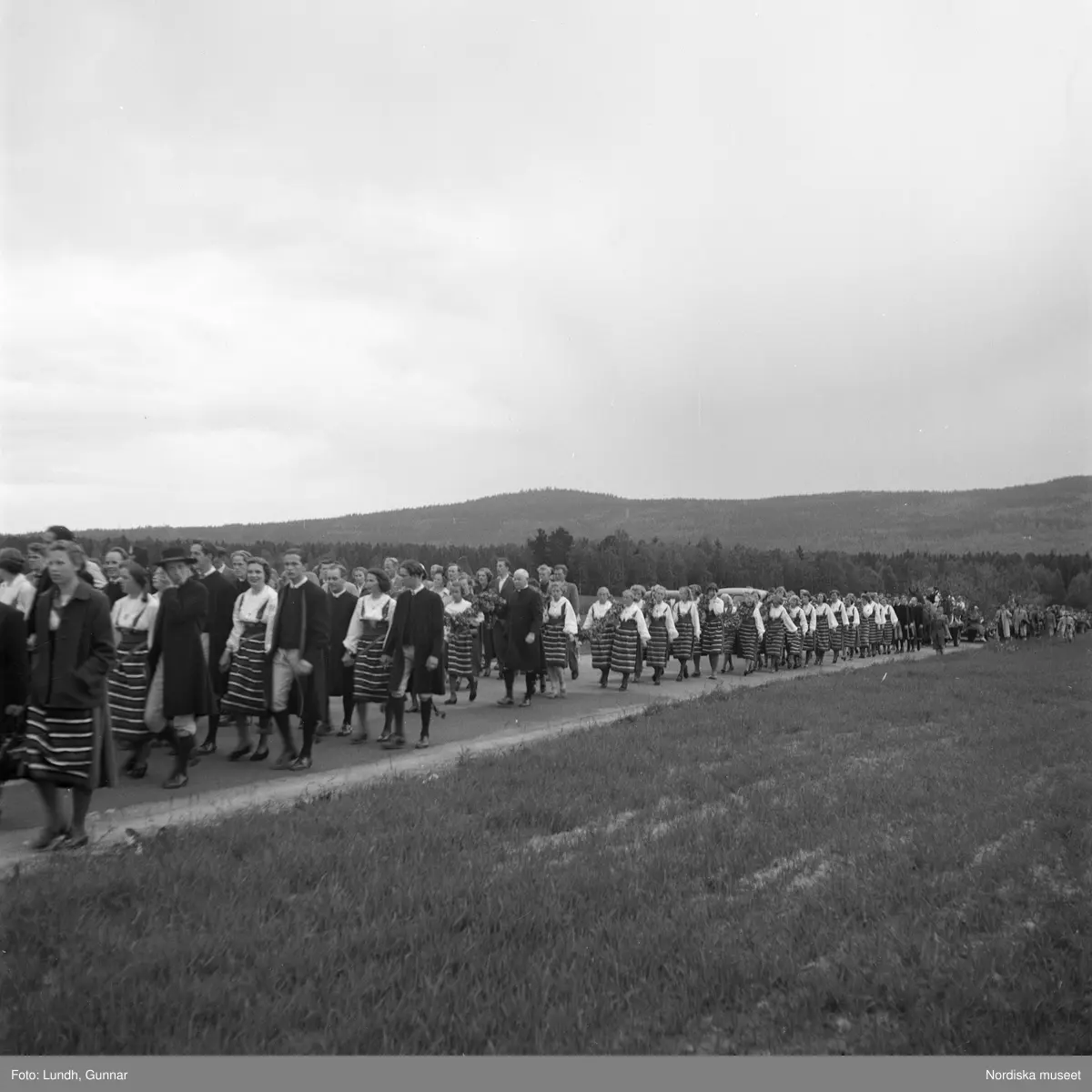 Motiv: (ingen anteckning) ;
Porträtt av en kvinna i folkdräkt och en man som sitter på marken, män och kvinnor i folkdräkt går i ett proccesionståg med flaggor och kvinnor bär en lövad girlang, människor åker på en hästdragen vagn, en folksamling går i ett processionståg.