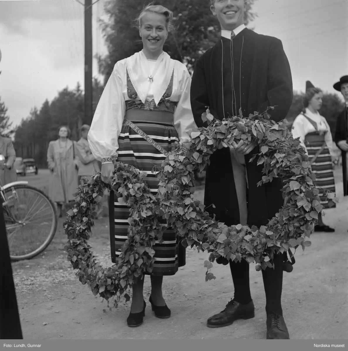 Motiv: midsommarfirande i Rättvik - Leksand ;
En pojke i folkdräkt och en flicka står vid en midsommarstång, en flicka pussar en pojke, en kvinna och en man handlar trasmattor av en man i en försäljningsvagn med text "Hemslöjd", en kvinna står vid en bil med kopparsaker till försäljning och en skylt "Ruben I Redin", en kvinna och en man i folkdräkt håller lövade ringar, kvinnor i folkdräkt går på en väg, en man kör en hästdragen vagn, ett led av kvinnor och män i folkdräkt bär en lövad girlang, människor åker på hästdragna vagnar.