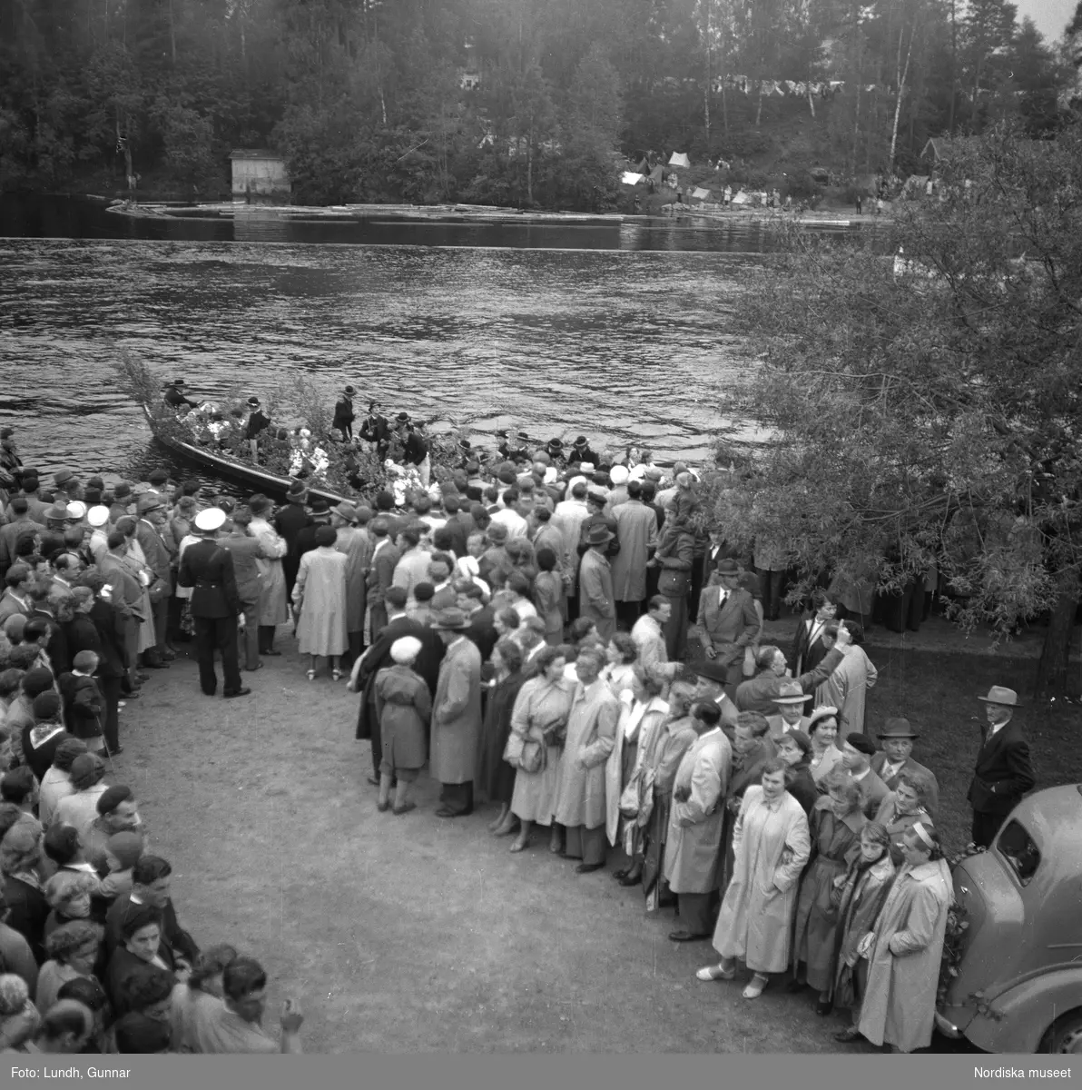 Motiv: (ingen anteckning) ;
En folksamling står kring en midsommarstång, en folksamling vid ett hus, en kyrkbåt ros av kvinnor och män i folkdräkt, en folksamling står vid en brygga med en kyrkbåt.