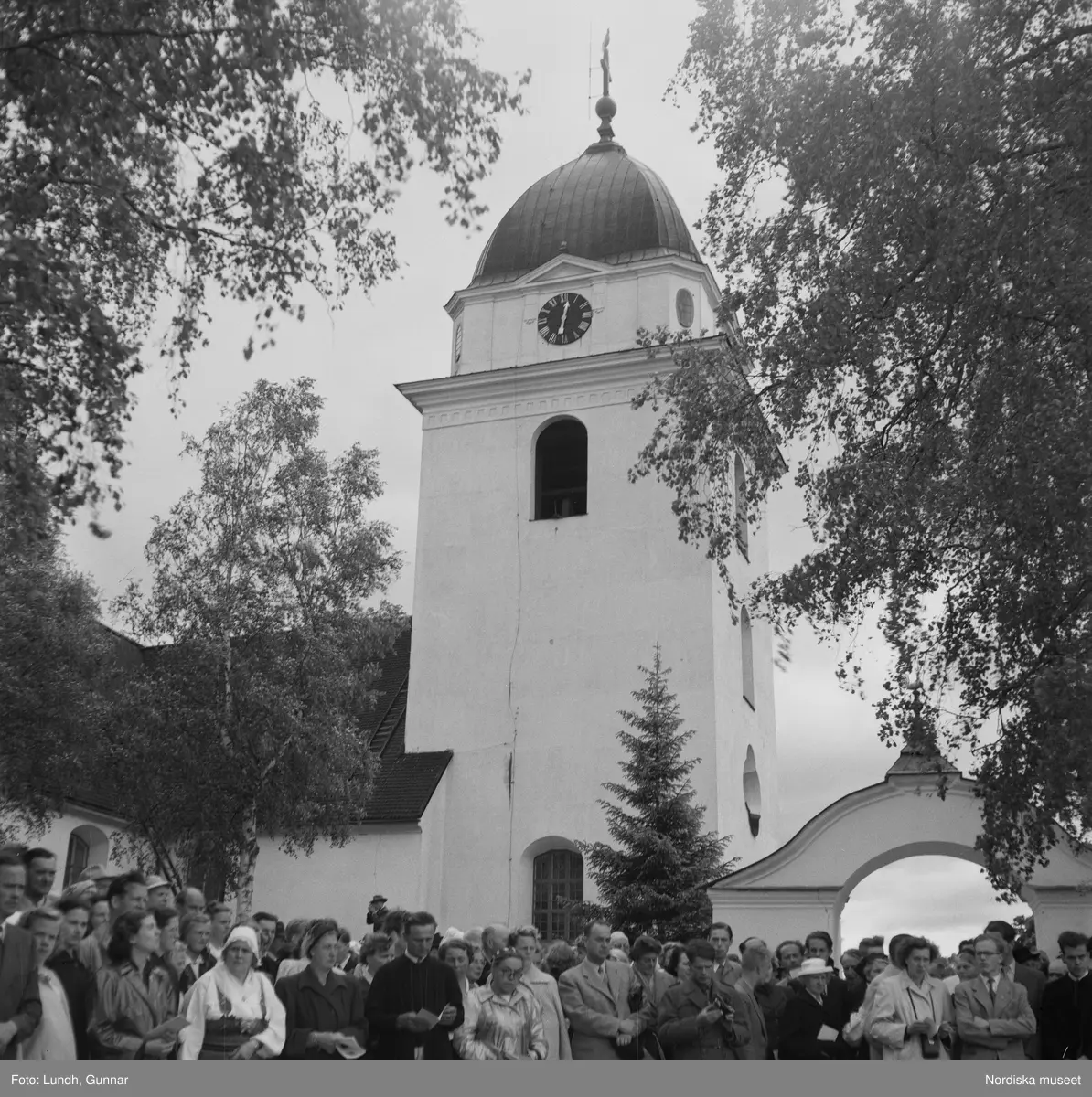 Motiv: (ingen anteckning) ;
En folksamling vid Rättviks kyrka, en folksamling står vid en brygga när kvinnor och män går ombord på två kyrkbåtar.