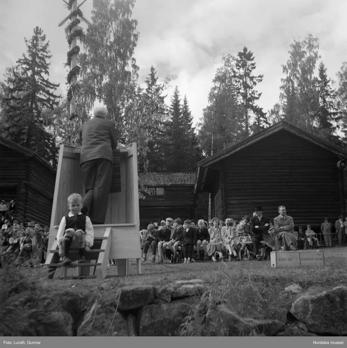 Motiv: (ingen anteckning) ;
Två män i folkdräkt håller fioler, en man i en talarstol talar till en folksamling, ett barn sitter på trapan till en talarstol, en folksamling vid en midsommarstång, porträtt av två varav ett i folkdräkt, kvinnor och män i folkdräkt dansar vid en midsommarstång.