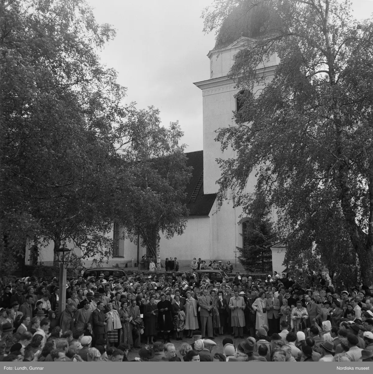 Motiv: (ingen anteckning) ;
En folksamling vid Rättviks kyrka, en folksamling står vid en brygga när kvinnor och män går ombord på två kyrkbåtar.