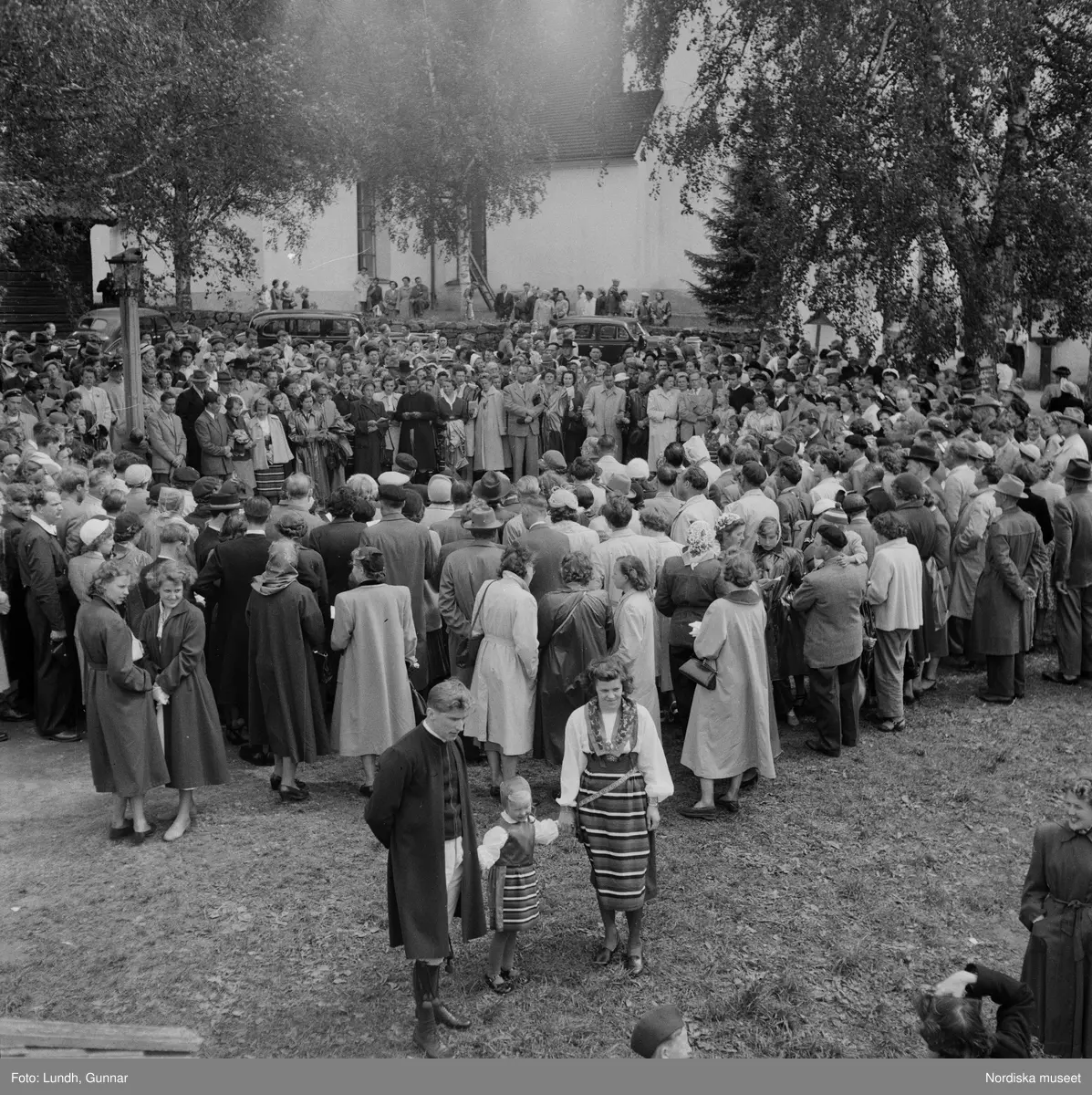 Motiv: (ingen anteckning) ;
En folksamling vid Rättviks kyrka, en folksamling står vid en brygga när kvinnor och män går ombord på två kyrkbåtar.