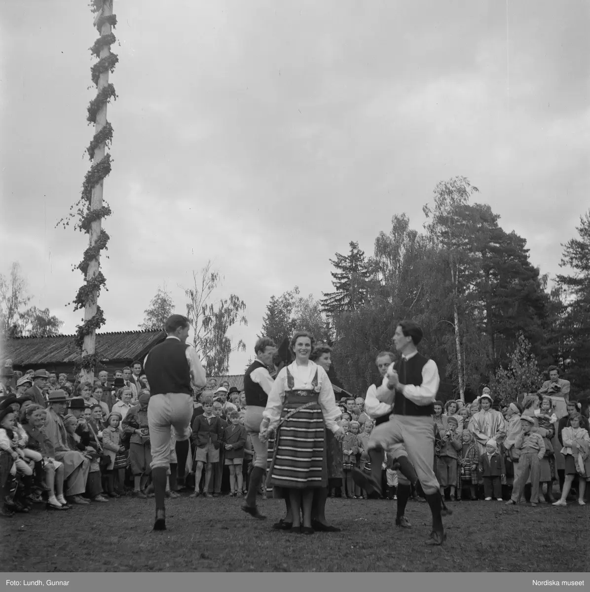 Motiv: (ingen anteckning) ;
Två män i folkdräkt håller fioler, en man i en talarstol talar till en folksamling, ett barn sitter på trapan till en talarstol, en folksamling vid en midsommarstång, porträtt av två varav ett i folkdräkt, kvinnor och män i folkdräkt dansar vid en midsommarstång.