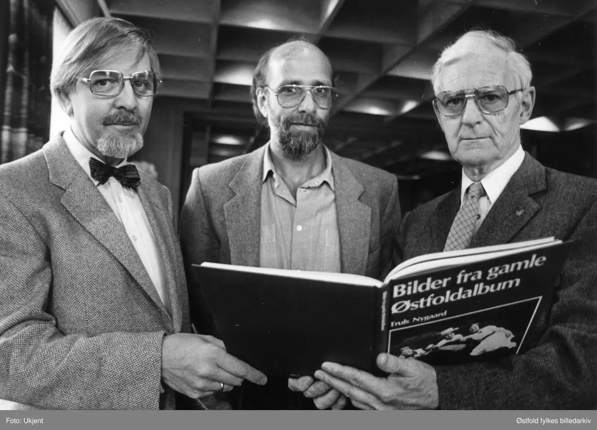 Lansering av boka "Bilder fra gamle Østfoldalbum" i 1984, av Truls Nygaard og Kjell Bertheau Johannessen. Ant. representant fra utgiver (ukjent), Landbruksforlaget, i midten. Fotograf Kjell til venstre og arkivleder Truls NYgaard til høyre, begge ansatt i ØStfold fylkes billedarkiv. 
HVOR?