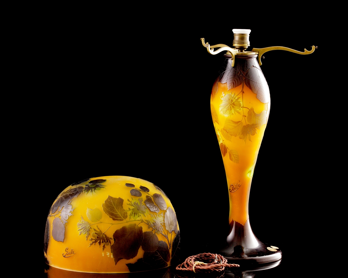 Opak lampa, gul med brunt och grönt växtmotiv i etsat överfång.
Metallfattning för glödlampa. Tvinnad textilsladd.
Etikett: rund: "GALLÉ PARIS NANCY ETABL.TS" Handskrivet i mitten: "23"
Etikett: oval: " ETABL.TS GALLÉ NANCY PARIS"