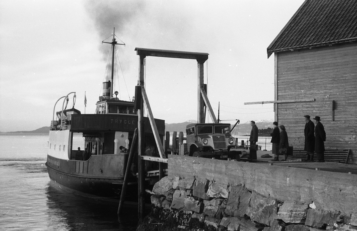 Avfotografert bilde av bilferja "Trygge" som iflg. Sveinung Berild betjente ferjesamband i Møre og Romsdal i over 50 år. Han forteller videre: "Den ble levert av Storviks Mek. Verksted, Kristiansund, i 1938. Den gikk i ruta Kristiansund-Bremsnes-Kvernes-Gjemnes-Torvikbukt til 1949. I tidsrommet 1949-1961 ble den brukt i ulike samband. 1961-1966 gikk den i det nyopprettet ferjesambandet på Vinjefjorden, Kristiansund-Engdal. I 1966 ble ferja ombygd, og overbygget ble erstattet av styrhus på styrbord side. Den fikk nå navnet "Vestra". Så gikk den i i en årrekke på Hjørundfjorden, og på 1980-tallet i samband i Aure og Molde-Bolsøya-Sekken.
I 1989 ble "Vestra" ombygd for å brukes som arbeidsbåt for ulike anlegg langs kysten. Ulike entreprenører ble eiere av ferja. Den var i bruk i Glomfjord i 2018, og er kanskje i drift enda."

Berild påpeker at å identifisere et gammeldags ferjeleie krever lokalkunnskap. Bildet i seg selv gir jo også få holdepunkter. At tidspunktet for originalen også er ukjent kompliserer ytterligere, men avfotograferingen skal være gjort for en ukjent oppdragsgiver i 1961.