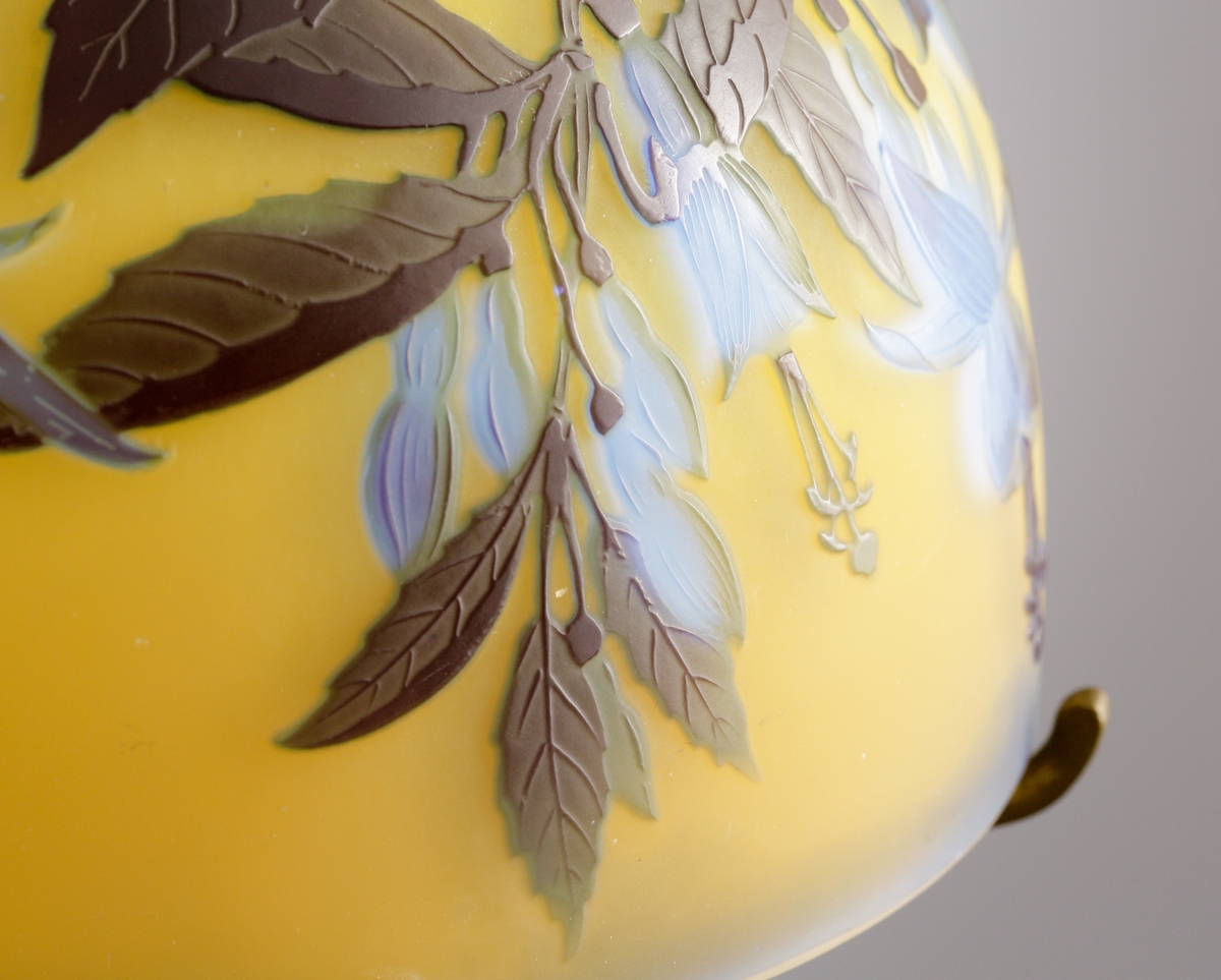 Gul opak lampa med växtmotiv. Etsat överfång i blått och gråbrunt.
Metallfattning för glödlampa. Tvinnad textilsladd.