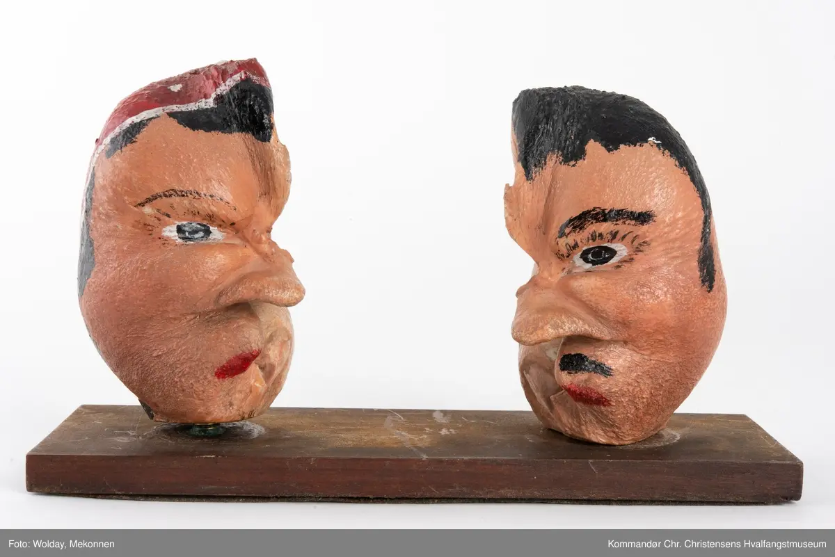 To bemalte øreknokler montert løst på en plate. De er malt som hode til en mann og en dame.