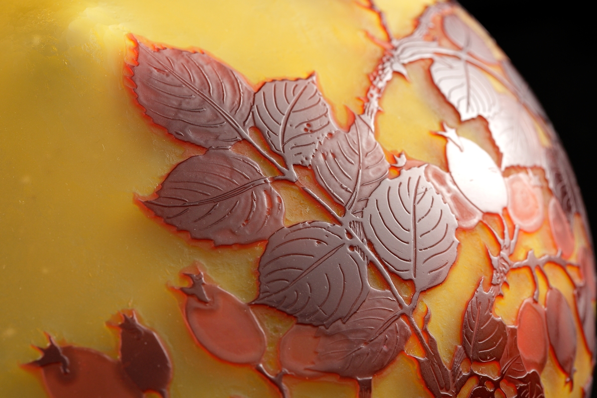 Lampa i skiftande gult, opakt glas. Dekor i rödbrunt etsat överfång. Motivet föreställer nyponkvistar.
Metallfattning för glödlampa. Tvinnad textilsladd.
Etikett: Skadad men "GALLÉ PARIS" kan uttydas.