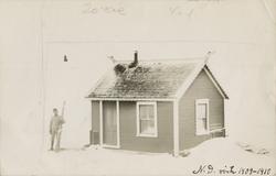 En mann med ski står ved et stovehus med dragehoder på endeg