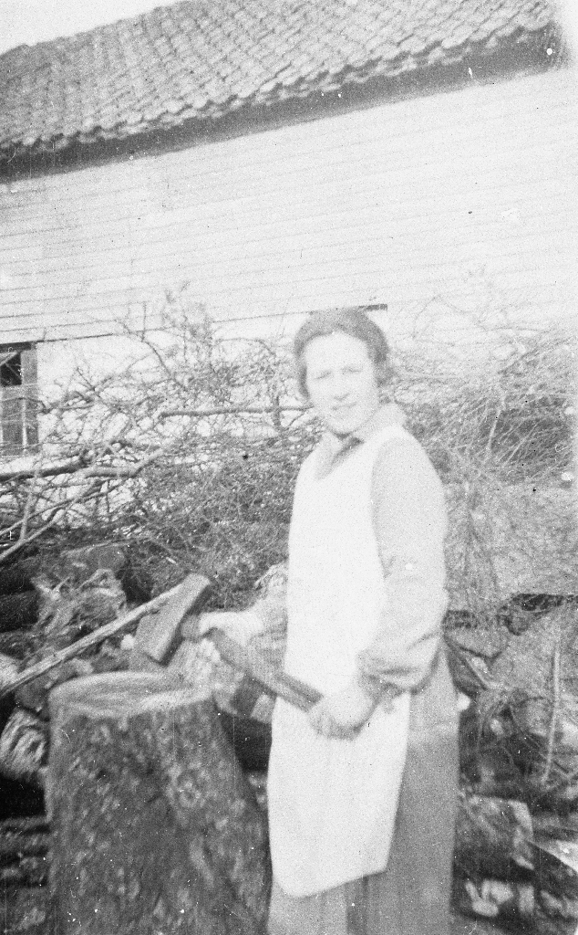 Tenestejente i arbeidsklær høgg ved. Det er Åsta Helene Soland (09.04.1904 - 11.09.1998) frå Marvik i Ryfylke. Ho tente hos Tønnes G. Kverneland og vart gift med sonen Trygve T. Kverneland i 1933.