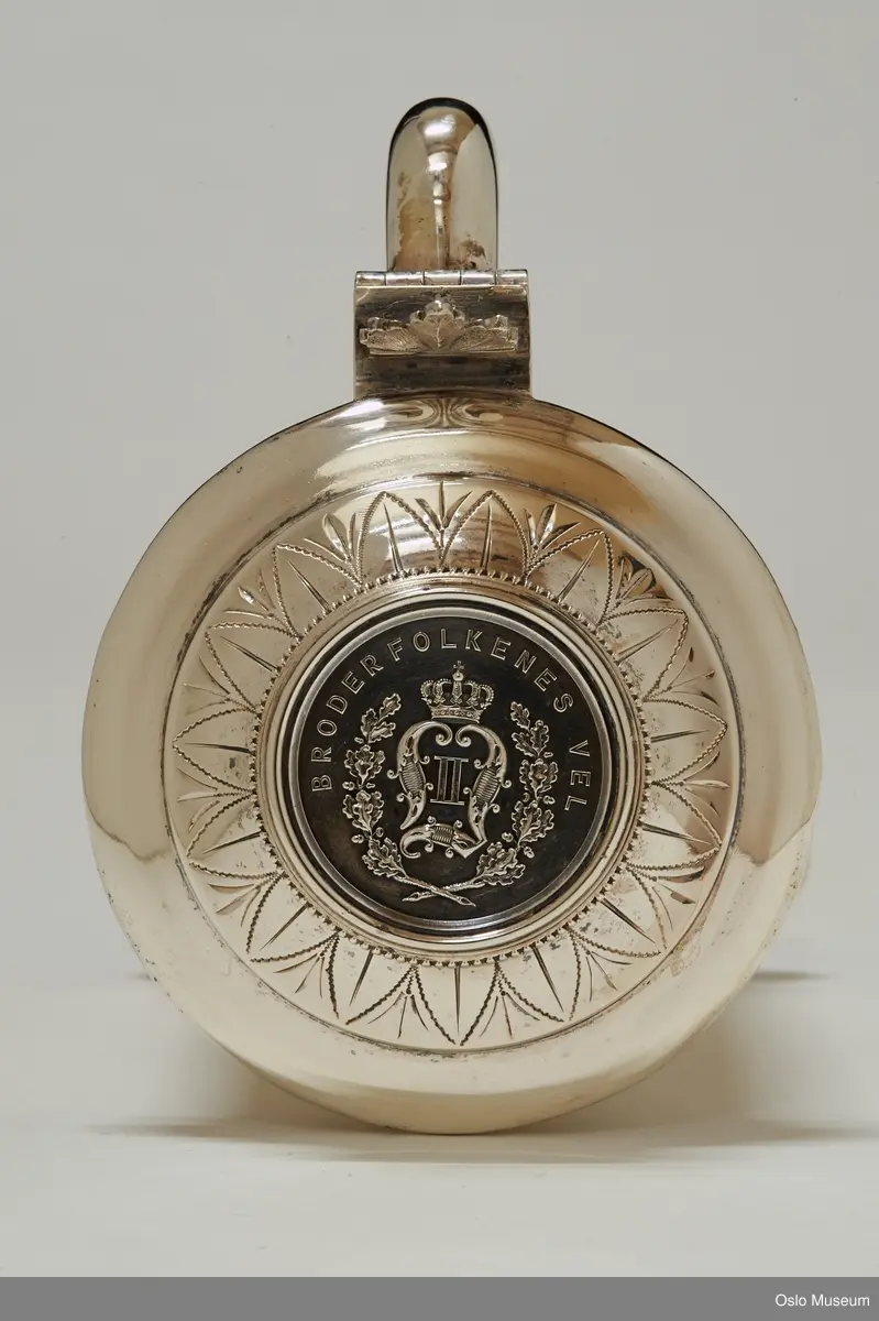Krus med lokk, som kan åpnes, tre ben, monogram på lokk, innskrift front.