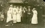 Vykort med motiv av ett antal vuxna och barn som ställt upp sig för fotografering. Enligt texten på baksidan: Fähusängar året 1922 i Wärsta parken i Njurunda. 6 aug. 1923.