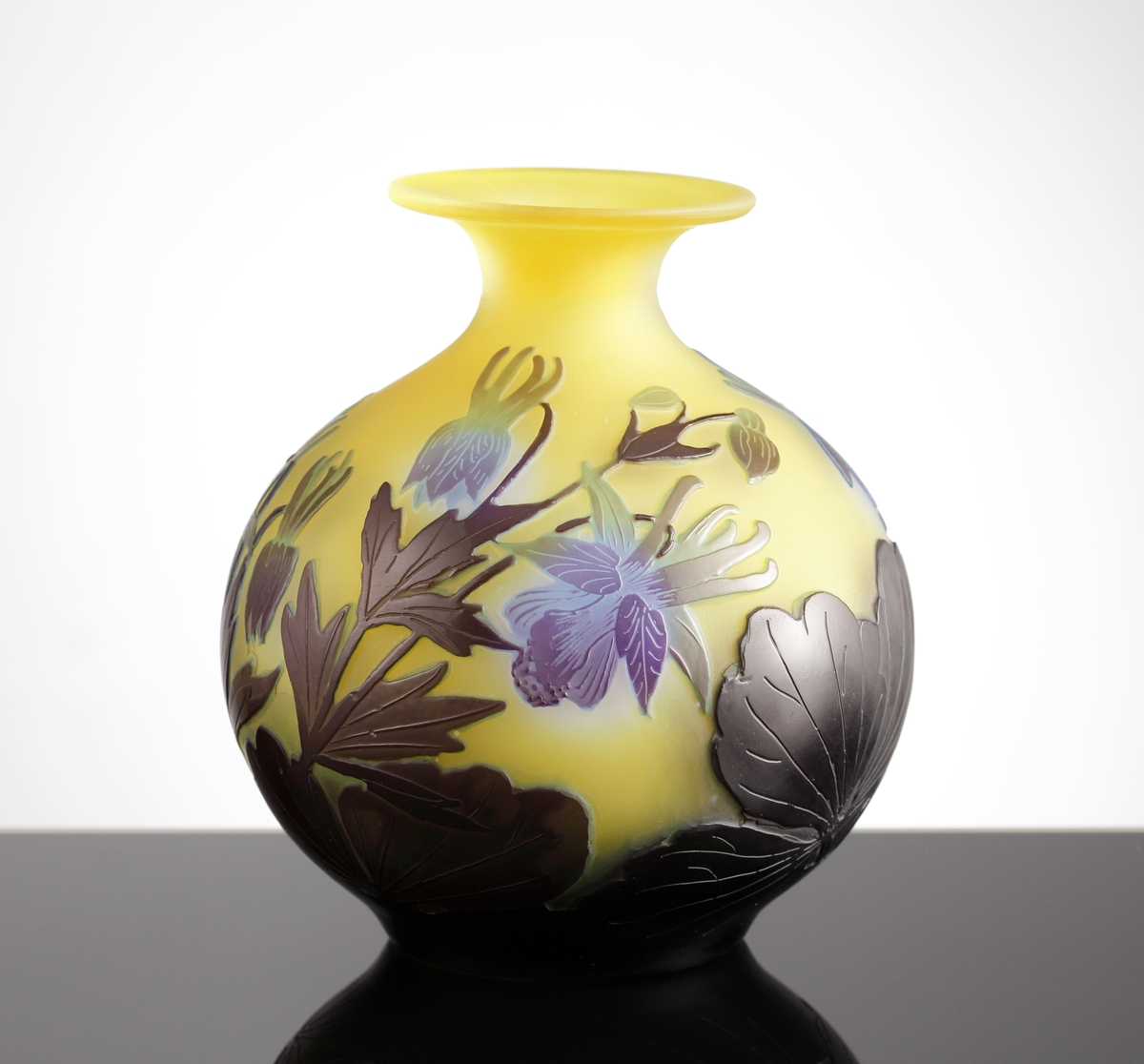 Halvopak, gul vas med etsat överfång i blå- och grönblå nyanser. Växtmotiv med blommor och blad.