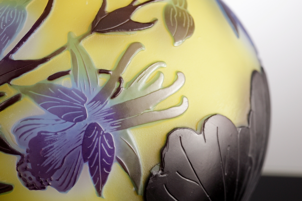 Halvopak, gul vas med etsat överfång i blå- och grönblå nyanser. Växtmotiv med blommor och blad.