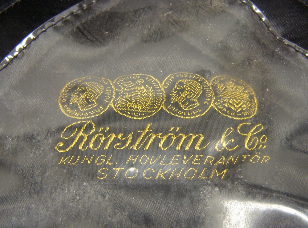 Skärmmössa med 35 mm svart jaquardvävt silkesband med invävda vinghjul.
1953 års broderade mössmärke.

Till mössan hör två medföljande sommarkapell, det ena med metallskena.