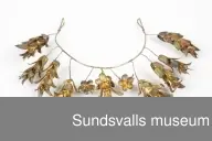 Diadem i böjd metalltråd med en ögla i var ände. Dekoration i form av metalltrådar med blommor och blad är fästade runt den böjda tråden.