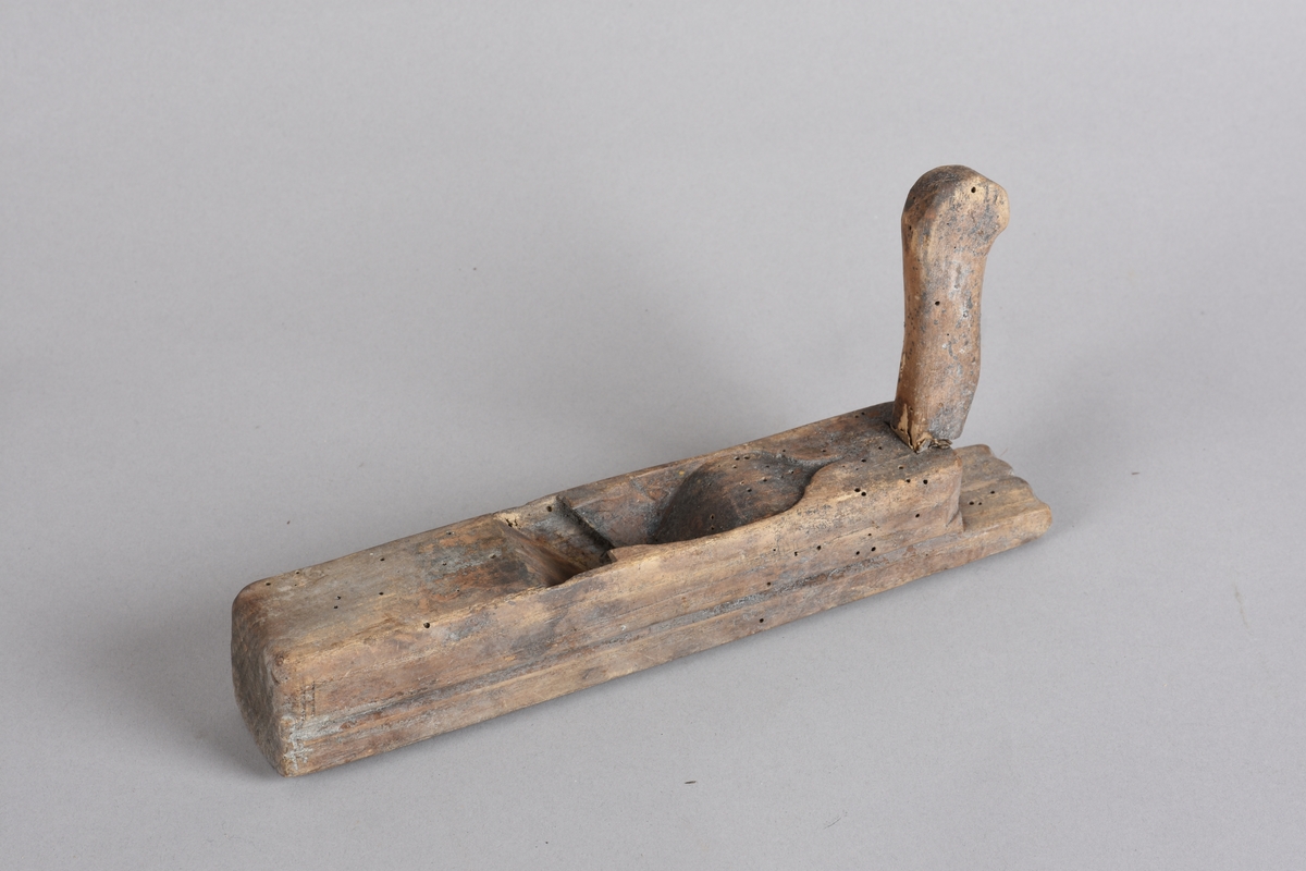 Høvel med rektangulær stokk, horn (handtak) med avrunda ende. Stokken er svakt runda på tvers på undersida. Har spor for høveljern og kile. Skoren dekor på toppen framom sponutkastet.