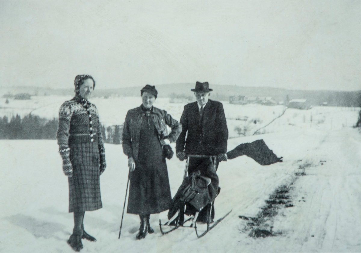 Gruppe 3 personer. Reidun Berg (født Olsen), Sigrid Olsen ( født Evenrud) og kjøpmann Johan Olsen på spark langs Fossbergetvegen i Vallset. Haraseth sees til høyre bak.